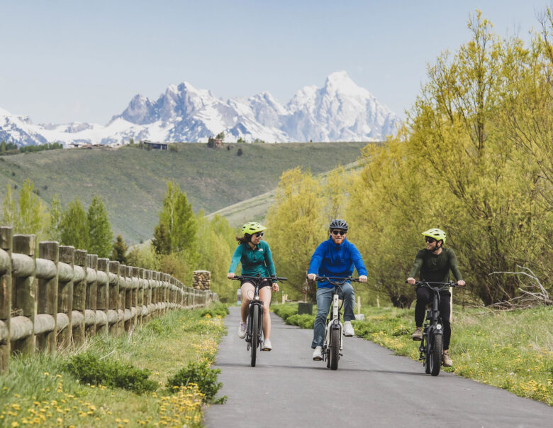 Three people riding E-Bikes on bike path with Teton mountain range in background